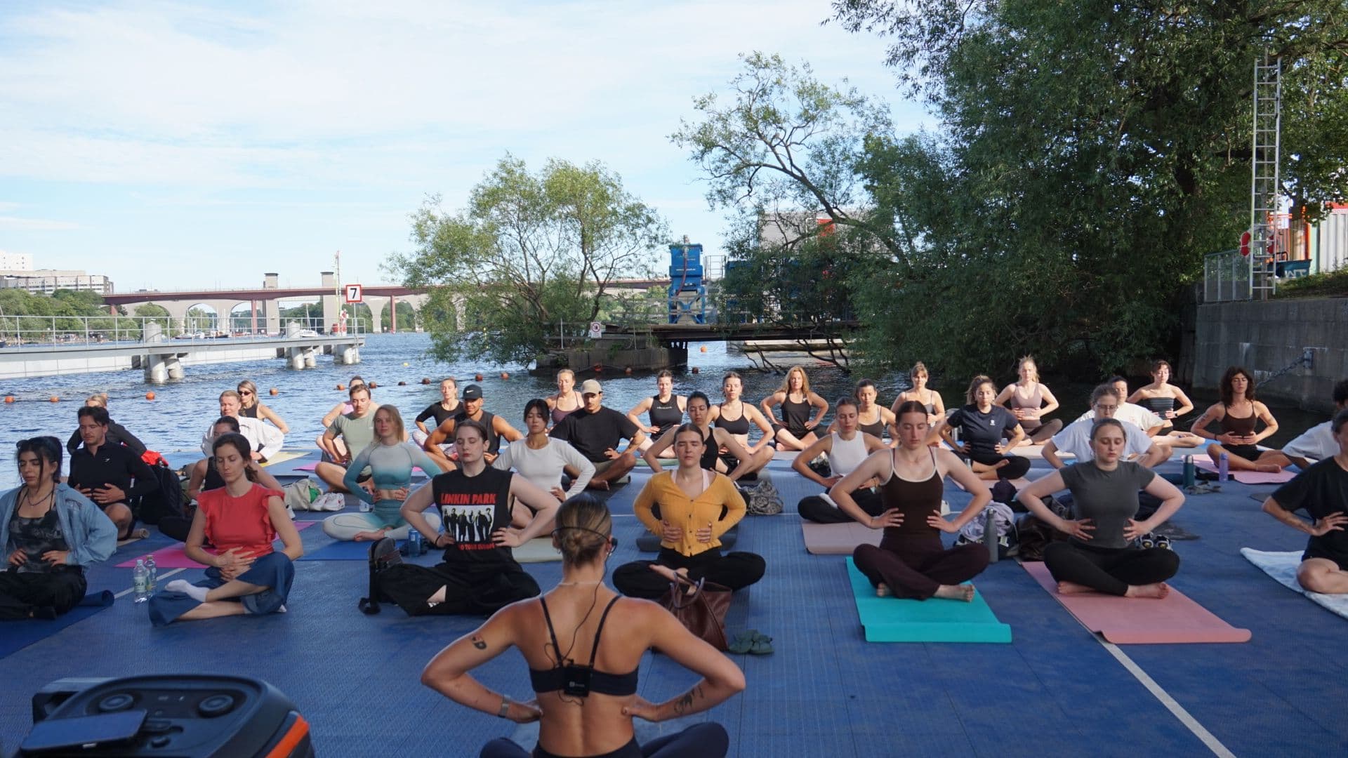 Vendela leder en stor grupp i yoga utomhus vid vattnet