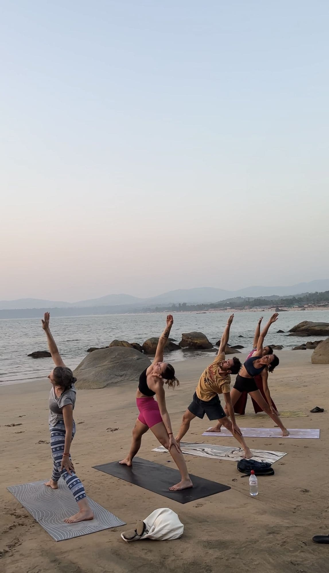 En grupp gör yoga tillsammans på en strand i morgonljus